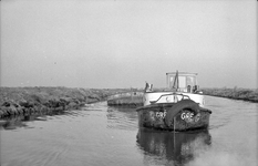 847511 Afbeelding van een sleepbootje dat een zandschip vol zand trekt, voor de aanleg van de P03 (de provinciale weg ...